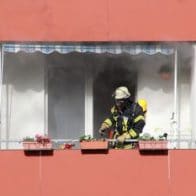 fire fighter standing on a balcony with smoke coming out from the window