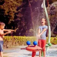 Little boy and girl play with splashes on water playground in summer park. hurt during a vacation