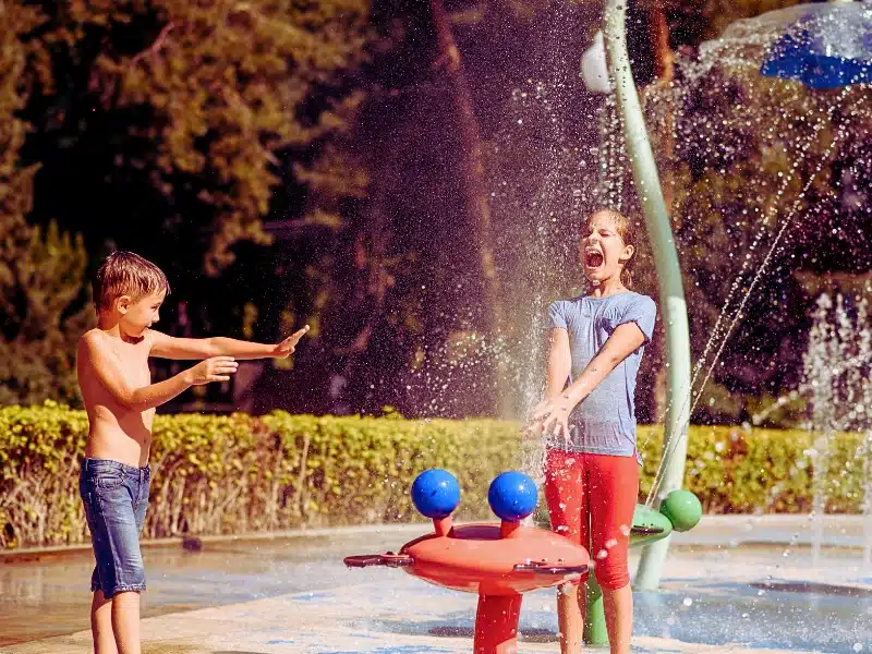 Little boy and girl play with splashes on water playground in summer park. hurt during a vacation