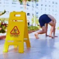 Caution wet floor signage and a man almost slipped in the background. File a Personal Injury Claim in Hawaii