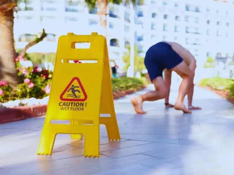 Caution wet floor signage and a man almost slipped in the background. File a Personal Injury Claim in Hawaii