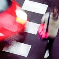 a blurred red car speeding past a pedestrian crosswalk while a person is walking across it.