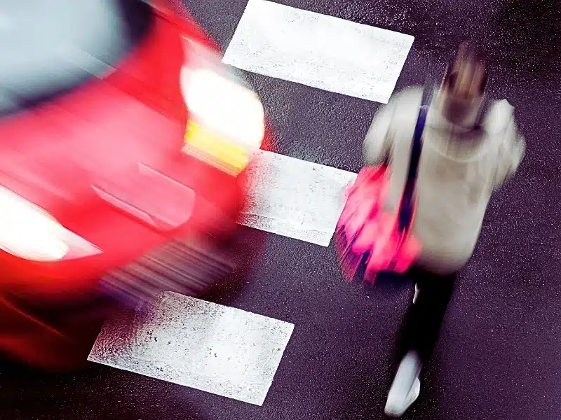 a blurred red car speeding past a pedestrian crosswalk while a person is walking across it.