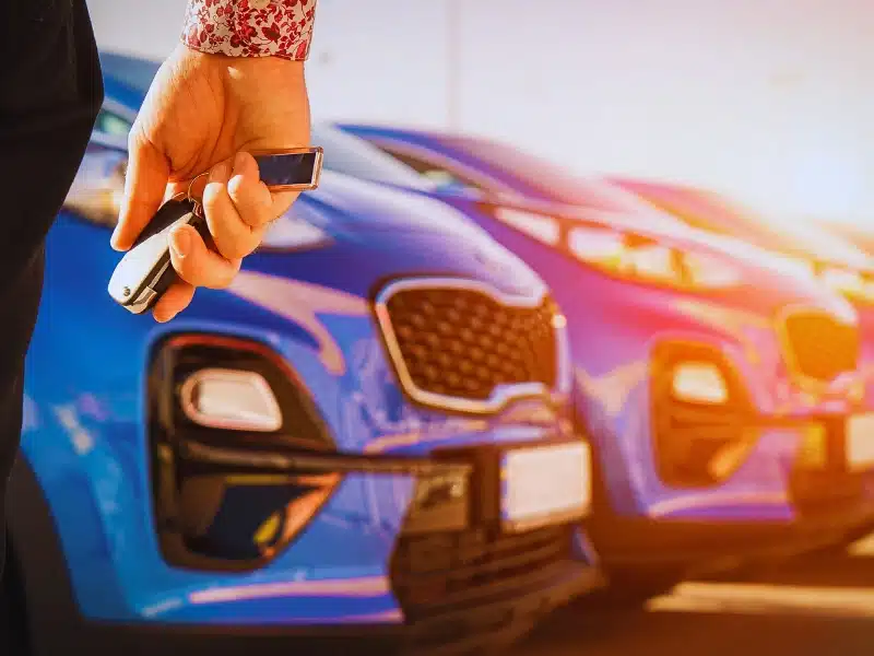 Hand holding car keys with blue cars behind. Rental Car Accidents